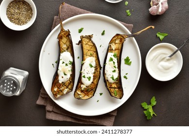 Roasted aubergine with garlic yogurt dressing on plate over dark background. Top view, flat lay - Powered by Shutterstock