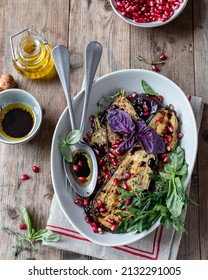 Roasted aubergine slices, served in a ceramic bowl with pomegranate seeds, olive oil, balsamic vinegar and fresh herbs. Vegetarian Food. Rustic wooden surface. Top view. Close up