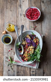 Roasted aubergine slices, served in a ceramic bowl with pomegranate seeds, olive oil, balsamic vinegar and fresh herbs. Vegetarian Food. Rustic wooden surface. Top view