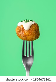 Roasted Baby Potatoes Stuck On A Fork, Isolated On A Green Background. Single Roasted Potato With Sour Cream Sauce And Herbs