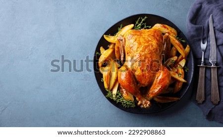 Roasted, baked chicken with potatoes and herbs on dark plate. Grey background. Copy space. Top view.