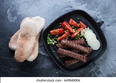 Roasted balkan cevapi on a grill pan and pita bread, top view on a grey stone background, horizontal shot