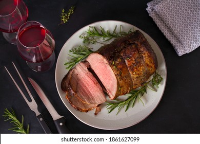 Roasted beef with herbs and red wine on dark background. View from above, top studio shot