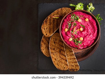 Roasted Beet Hummus with toast in a ceramic bowl on a dark background. Top view