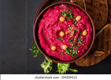Roasted Beet Hummus with toast in a ceramic bowl on a dark background. Top view