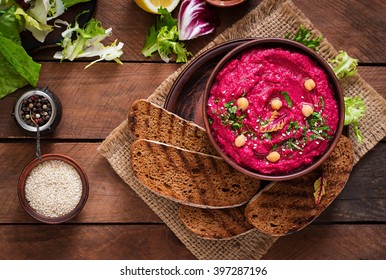 Roasted Beet Hummus with toast in a ceramic bowl on a wooden background. Top view
