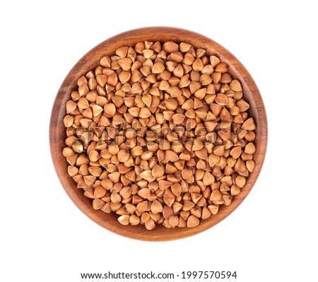Roasted buckwheat grains in wooden bowl, isolated on white background. Dry brown buckwheat groats. Top view.