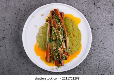 Roasted Carrots Are Served On A White Stoneware Plate Alongside A Pesto