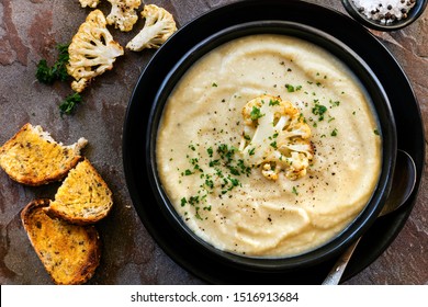 Roasted cauliflower soup in rustic black bowl, with crusty sourdough toast.  Top view.