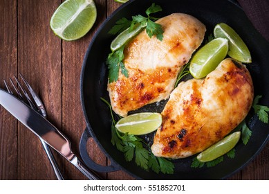 Roasted chicken breasts with lime and parsley on dark wooden background top view. Healthy food. Meat