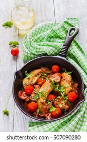 Roasted chicken fillet, cooked with mushrooms, garlic, paprika and olive oil. Cast-iron skillet and fresh cherry tomatoes on wooden table, top view.