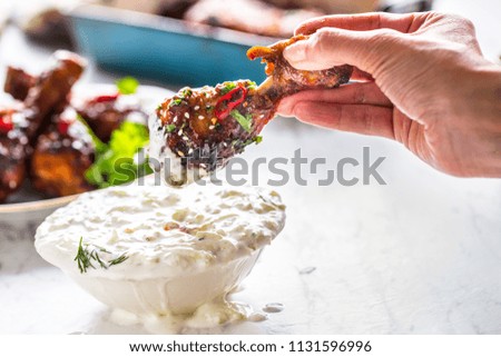 Roasted chicken legs in woman hand and tzatziki dip sauce or dressing.