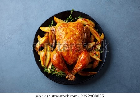 Roasted chicken with potatoes on dark plate. Grey background. Close up. Top view.