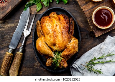 Жареная курица с розмарином подается на черной тарелке с соусами на деревянном столе, вид сверху