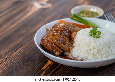 Roasted chicken thighs and drumsticks are served with jasmine rice and fresh vegetables in a white plate. Chicken thighs baked in sweet and delicious sauce are served with hot steamed rice on a plate.