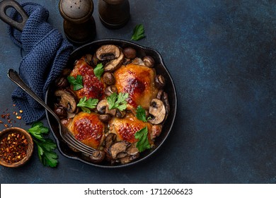 roasted  chicken thighs with mushrooms on cast iron  pan , dark blue concrete background, top view, copy space