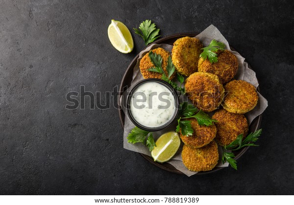 roasted chickpeas falafel patties with garlic\
yogurt sauce. Top view. black\
background