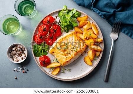 Roasted cod, codfish with baked potatoes and cherry tomatoes on plate. Grey background. Top view.