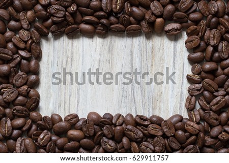 Roasted cofee beans around square space of wood, top view