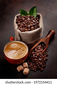 Roasted Coffee Beans In Burlap Bag, Brown Sugar And Cup Of Hot Espresso Coffee On Stone Table