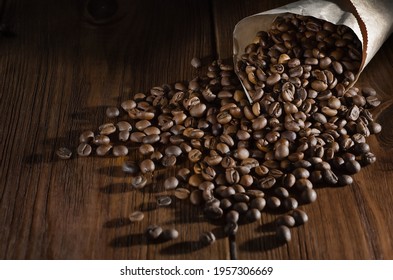 Roasted Coffee Beans Lie In A Paper Bag And Are Scattered On A Wooden Background. View From Above