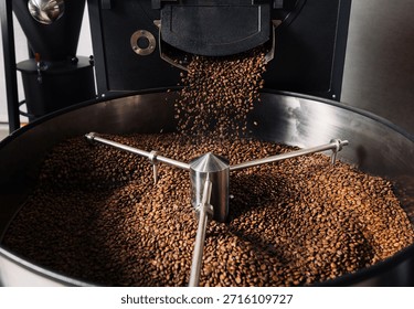 Roasted coffee beans are pouring from a machine in a manufacturer's