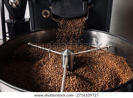 Roasted coffee beans are pouring from a machine in a manufacturer's