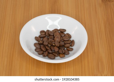 Roasted Coffee beans in a white bowl with a wooden background