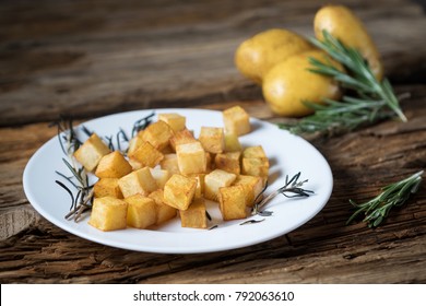 roasted diced potatoes with rosemary and olive oil on the plate on wooden background