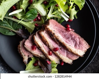 Roasted Duck Breast With Green Salad And Pomegranate On Black Plate. Overhead View.