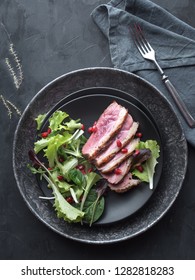 Roasted Duck Breast With Green Salad And Pomegranate On Black Plate. Overhead View.