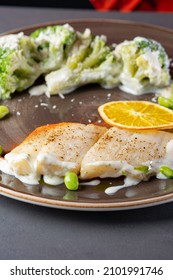 roasted fish (pike or walleye) with fried broccoli in cream sauce on a plate on a stone background