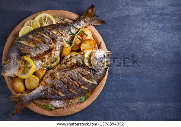 Roasted fish and potatoes, served on\
wooden tray. overhead, horizontal, copy space -\
image