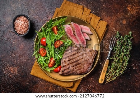 Roasted Flank or Flap Steak in a plate with salad. Dark background. Top view