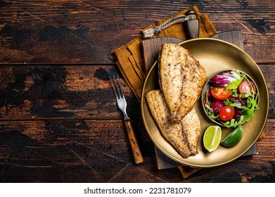 Roasted Gilthead Sea Bream fillets served with fresh vegetable salad. Wooden background. Top view. Copy space.