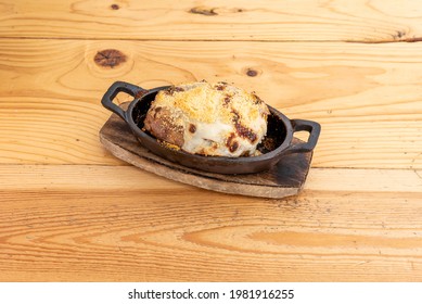 Roasted And Gratin Potato With Béchamel Sauce And Grated Cheese Inside An Individual Cast Iron Container On Wooden Table