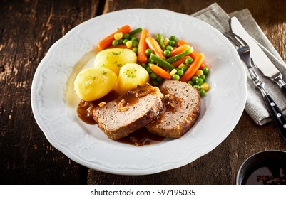 Roasted Ground Pork And Beef Meat Loaf And Gravy With Mixed Fresh Vegetables On A Generic White Plate With Utensils On A Rustic Table