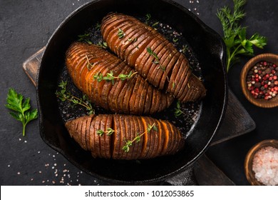 roasted hasselback sweet potato on cast iron pan. Dark background, top view