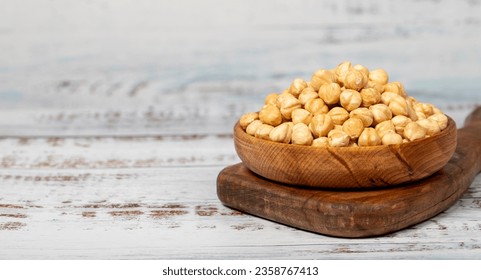 Roasted hazelnuts in wood bowl. Peeled hazelnuts kernel on white wood background. Copy space. Empty space for text