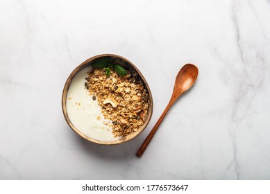 Roasted Healthy Homemade Granola With Gluten Free Rolled Oats Or Porridge Oats, Variety Of Chopped Nuts And Seeds, And Maple Syrup. Portion Of Granola And Kefir Or Yogurt In Coconut Bowl