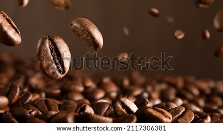 Roasted hot coffee beans falling on pile of coffee beans. Front view. Horizontal composition.