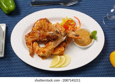 Roasted Jumbo Prawns  With Salt, Pepper, Sauce  And Fresh Vegetables On White Oval Plate, Isolated On Blue Background, Low Angle Back Side View, Macro Close-up Focus At The Middle Of Food 