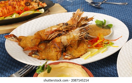 Roasted Jumbo Prawns  With Salt, Pepper, Sauce  And Fresh Vegetables On White Oval Plate, Isolated On Blue Background, Low Angle Back Side View, Macro Close-up Focus At The Middle Of Food 