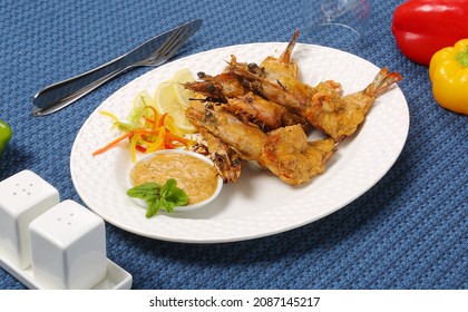 Roasted Jumbo Prawns  With Salt, Pepper, Sauce  And Fresh Vegetables On White Oval Plate, Isolated On Blue Background, Low Angle Back Side View, Macro Close-up Focus At The Middle Of Food 