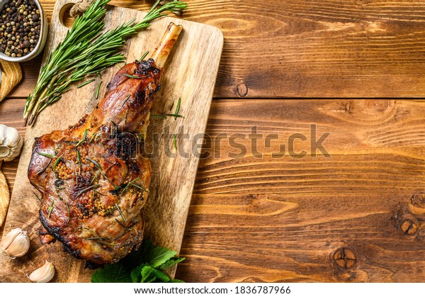 Roasted lamb, sheep leg\
on a cutting board with rosemary. wooden background. Top view. Copy\
space