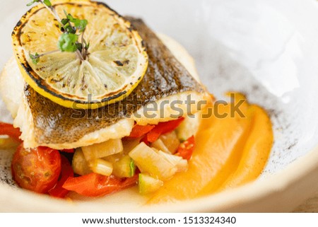 Roasted pike perch or cod fish with baked vegetables. Dish decorated with a slice of lemon. Restaurant menu