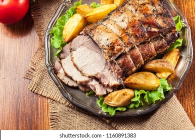 Roasted pork loin with baked potatoes and herbs on a plate
