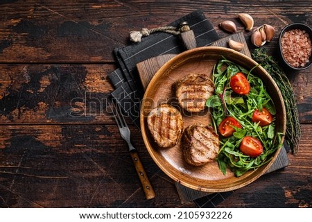 Roasted pork medallions steaks from tenderloin fillet with vegetable salad in wooden plate. Wooden background. Top view. Copy space