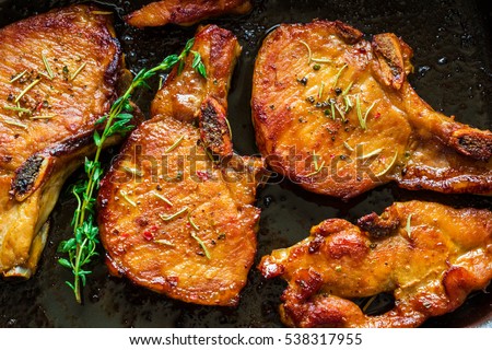 Roasted pork steaks, cutlets with bones  and thyme on black baking sheet, top view.