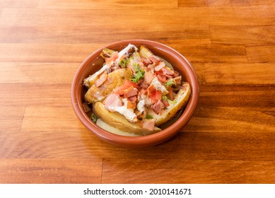 Roasted potato salad with skin, fried bacon in pieces, diced tomatoes with cream cheese on clay pot